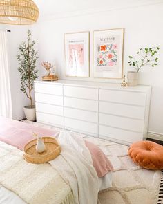 a bedroom with white furniture and pink accessories on the bed, along with two framed pictures