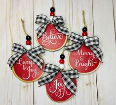 four christmas ornaments hanging on a white wooden background with the words believe, merry and bright