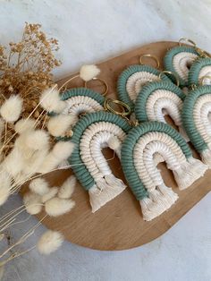 four pairs of earrings with tassels are on a wooden board next to dried flowers