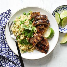 a white plate topped with meat and rice next to lime wedges on a blue and white napkin