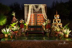 an outdoor stage decorated with flowers and candles for a wedding reception at night, surrounded by potted plants