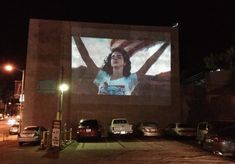 a large screen on the side of a building with cars parked in front of it