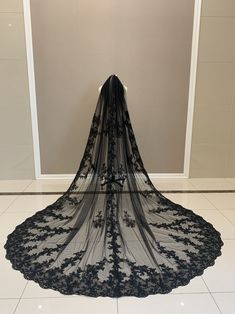 a black wedding veil with flowers on the bottom is laying on the floor in front of a wall