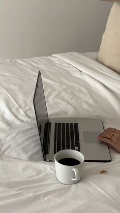 a laptop computer sitting on top of a white bed next to a cup of coffee