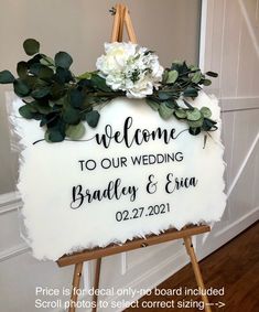 a welcome sign with flowers and greenery hanging from it's easel in front of a door