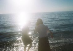 two people are playing in the water at the beach while sun shines on them