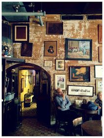 two men are sitting at a table in front of a wall with pictures on it