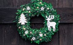 a green wreath with white deer and trees on it, hanging from a wooden door