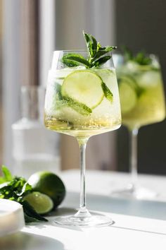 two glasses filled with cucumber, mint and lemonade on a white table