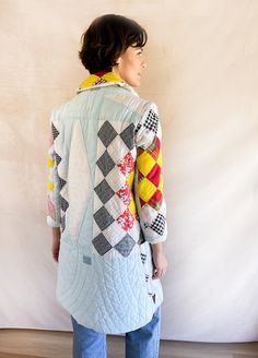 a woman standing in front of a white wall wearing a jacket with colorful patches on it