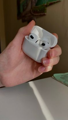 a hand holding an airpods with two eyes on it's side and one eye open