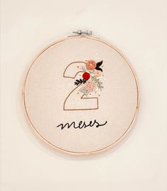 the number two embroidered into a hoop with flowers and leaves on it's side