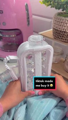 a person holding up a baby bottle in front of a pink mixer and other items