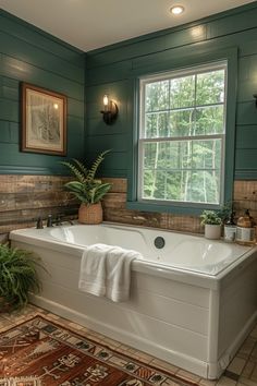 a bath tub sitting under a window next to a rug and potted plant in a bathroom