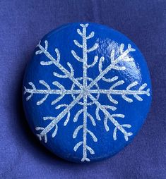 a blue rock with white snowflakes painted on it, sitting on a purple surface