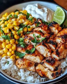 a white bowl filled with rice, corn and chicken next to a lime wedge on the side