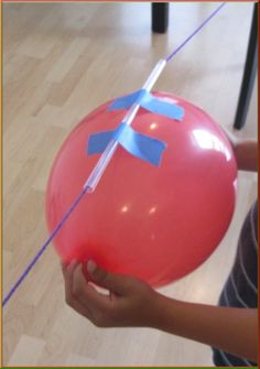 a person holding a large red balloon with blue tape on it's end and an arrow sticking out of the balloon