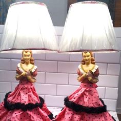 two lamps that are sitting on top of a table next to each other, one is wearing a pink dress and the other has a black ruffled skirt