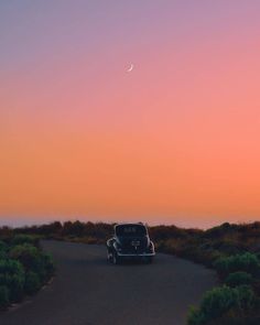 an old car driving down the road at sunset