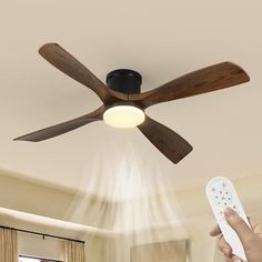 a person holding a remote control in front of a ceiling fan with light coming from it