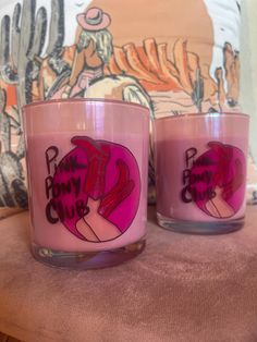 two pink candles sitting next to each other on top of a table in front of a pillow