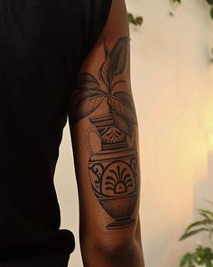 a man with a tattoo on his arm holding a potted plant in front of him