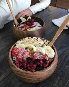 two bowls filled with fruit and nuts on top of a wooden table next to a person