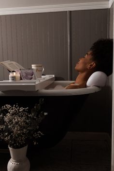 a woman laying in a bathtub next to a vase with flowers