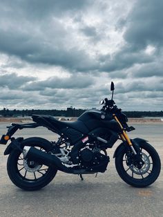 a black motorcycle parked on top of a parking lot next to a cloudy blue sky