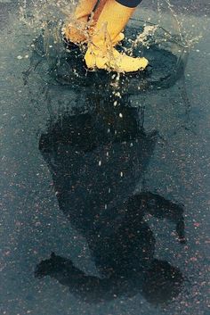 a person in yellow boots splashing water onto the ground with their feet and legs