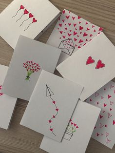 several cards with hearts and flowers on them sitting on top of a wooden table next to each other