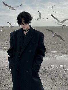 a man standing on the beach with seagulls flying around him and his face obscured by his coat