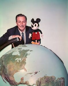 a man sitting on top of a globe with a stuffed animal in front of him