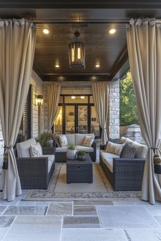 an outdoor living area with couches, chairs and curtains on the outside wall is lit by recessed lights