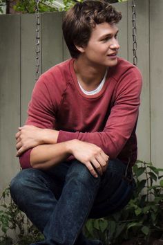 a young man sitting on top of a wooden bench next to a green planter