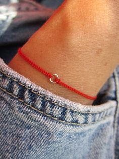 a person wearing a red string bracelet with a silver ring on it's wrist