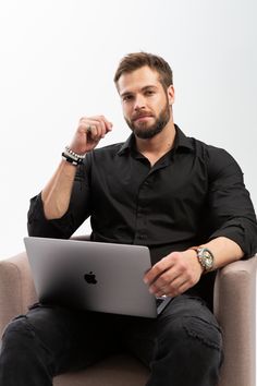 a man sitting in a chair with a laptop computer on his lap and looking at the camera