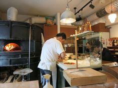 a man cooking food in a kitchen next to an open fire place with lights hanging from the ceiling