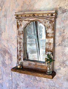 a vase with flowers sitting on top of a shelf next to a mirror that has shutters in it