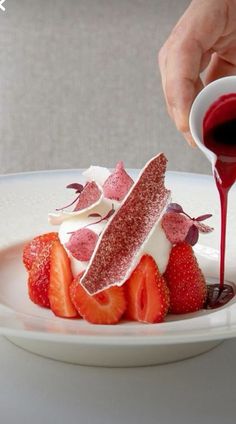 someone is pouring sauce on some strawberries in a plate with other foods and desserts