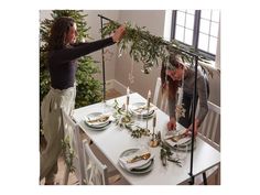 two people standing over a table with plates on it and greenery hanging from the ceiling