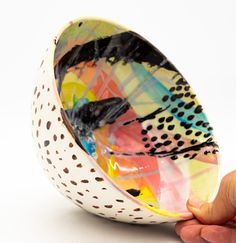 a hand is holding a colorful bowl with black dots and spots on it's rim