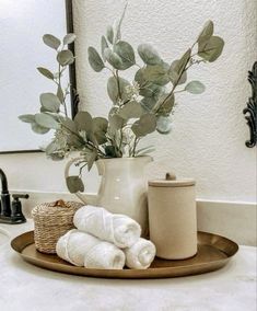 a bathroom sink topped with a white vase filled with flowers and towels next to a mirror