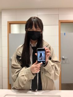 a woman wearing a black mask and holding up a cell phone in front of her face