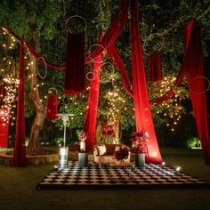 an outdoor wedding setup with red drapes and lights on the trees, checkerboard floor