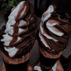 two ice cream sundaes with chocolate and whipped cream on top are being held by someone's hands