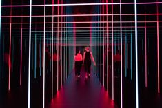 two people walking down a dark hallway with neon lights on the walls and flooring