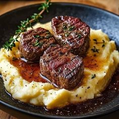 three steaks and mashed potatoes on a black plate