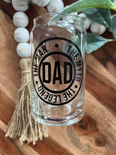 a glass with the words dad on it next to some white beads and a green plant