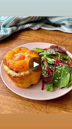 a white plate topped with a pastry next to a salad on top of a wooden table